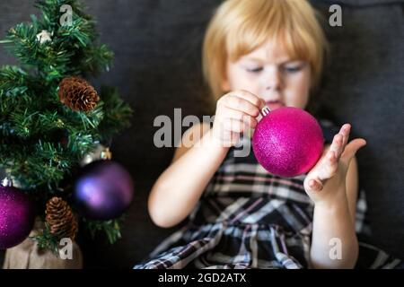 Boule d'arbre de Noël dans les mains des enfants. Petite blonde belle fille décorant arbre de Noël à la maison Banque D'Images