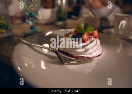 Dessert meringue gâteau Pavlova avec des fraises fraîches, des bleuets et des feuilles de menthe sur une assiette en céramique blanche. Banque D'Images