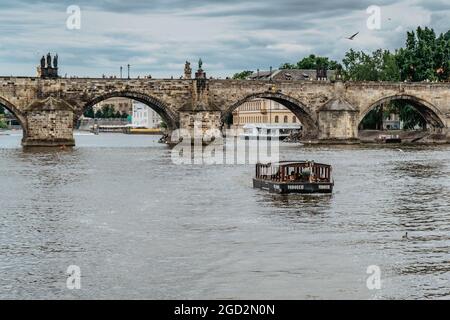 Prague, République tchèque-août 4,2021. Petit ferry en bois avec des passagers traversant la rivière Vltava, pont Charles en arrière-plan.transport local d'eau Banque D'Images