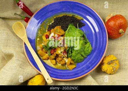 Vue de dessus du curry avec du poulet à la mangue et des lentilles noires sur une assiette bleue avec une cuillère en bois Banque D'Images