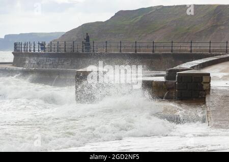 Homme pêchant avec des vagues s'écrasant contre les défenses de mer dans le Yorkshire de Scarborough Banque D'Images