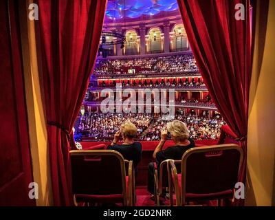 ALBERT HALL CAISSON PERFORMANCE INTÉRIEUR deux dames regardant un spectacle à travers des lunettes d'opéra dans une boîte privée en velours rouge avec des rideaux moelleux au Royal Albert Hall Kensington Londres Banque D'Images