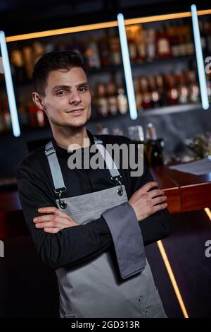 Beau barman en tablier debout au comptoir du bar Banque D'Images