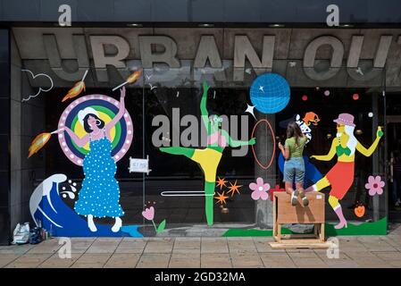 Une jeune femme peint des figures colorées sur la fenêtre du magasin Urban Outfitters sur Princes Street, Édimbourg, Écosse, Royaume-Uni. Banque D'Images