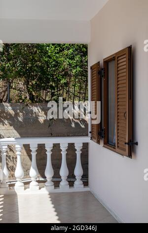 Terrasse blanche d'architecture grecque classique avec balusters et fenêtre avec volets. Vue sur la verdure dans l'ombre. L'été dans la maison de campagne près d'Ath Banque D'Images
