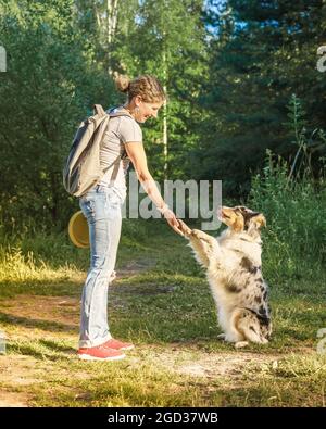 Chien de race mixte enjoué donnant patte à une femme d'âge moyen heureuse pendant la marche dans le parc Banque D'Images