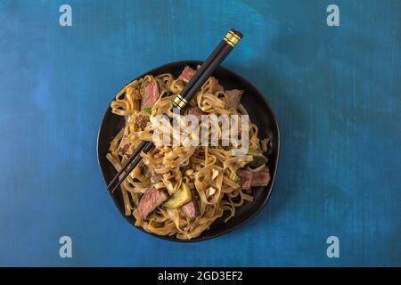 Un bol de nouilles asiatiques avec des tranches de steak, des nouilles de riz et des légumes Banque D'Images