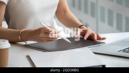 Jeune femme d'affaires mains tenant le stylet stylet et travaillant sur tablette numérique noire PC avec ordinateur portable sur le bureau à la maison moderne. À distance Banque D'Images