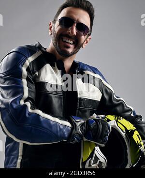 Joyeux sourire barbu homme motard en moto cuir veste et gants tient son casque et rires Banque D'Images