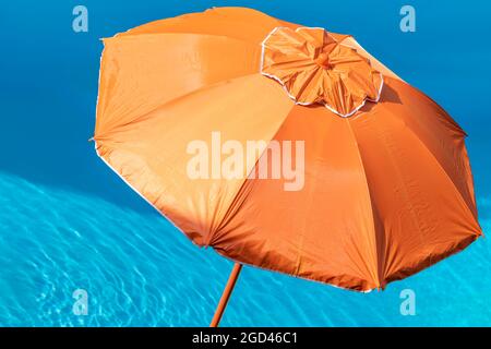 Un parasol orange sur la plage contre l'eau bleue et claire d'une piscine Banque D'Images