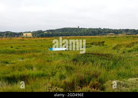 Un petit canot bleu déserté dans le marais du milieu près de la rivière Glaven à Blakeney Eye, Blakeney, Norfolk, Angleterre, Royaume-Uni. Banque D'Images