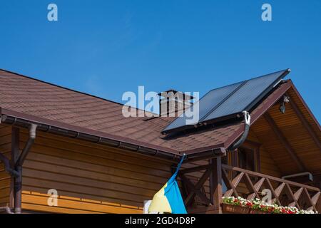 Système de chauffage individuel thermique solaire pour l'eau chaude sur le bitume asphalte bardeaux toit. Cheminée en briques sur une maison en bois. Gouttière. Banque D'Images