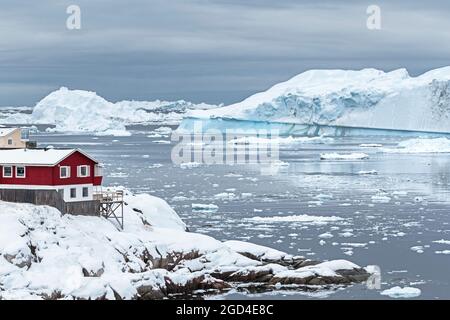 Une maison de ville rouge se dresse sur la rive en hiver.Ilulissat, baie de Disko, Groenland Banque D'Images