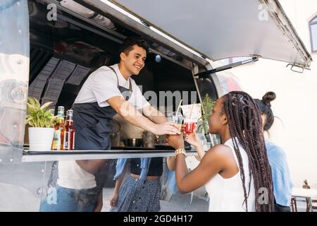 Deux clients reçoivent des boissons du propriétaire du camion. Un vendeur joyeux qui regarde les clients. Banque D'Images