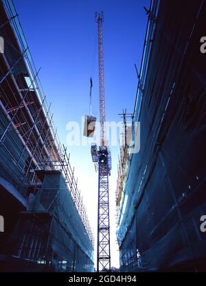 Regardant vers une grue à tour soulevant des matériaux de construction dans les airs, sur un chantier de construction à Londres, entouré d'échafaudages. Banque D'Images