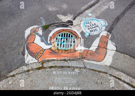 Une peinture intelligente d'une cloche de plongée sur une grille d'égout métallique au-dessus d'un drain de tempête dans un coin de rue à Fairbanks, Alaska. Banque D'Images