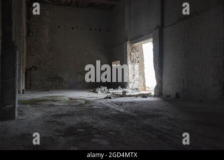 Intérieur industriel abandonné. Entrepôt vide sombre avec des murs en béton fissurés, des briques cassées et de la lumière tombant par la porte ouverte Banque D'Images