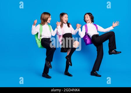 Photo d'enfants adorables vêtements d'école sacs à dos souriants marchant tenant les bras montant poings isolé couleur bleu fond Banque D'Images