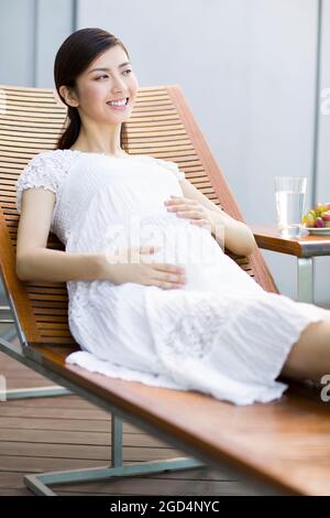 Bonne femme enceinte se détendant sur une chaise longue Banque D'Images