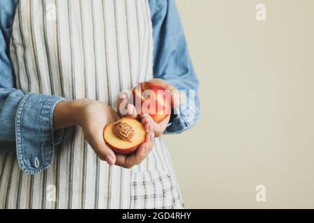 Une fille en tablier tient des fruits de pêche mûrs Banque D'Images