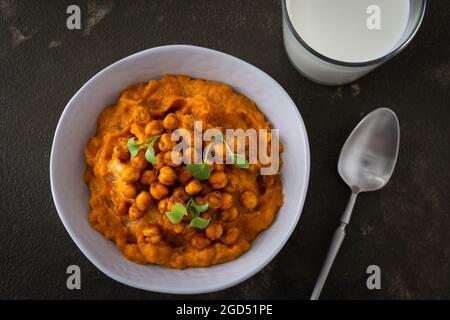 Soupe de potiron épaisse aux pois chiches cuits et aux pousses de radis dans une assiette avec un verre de lait sur la table, délicieux dîner sain Banque D'Images