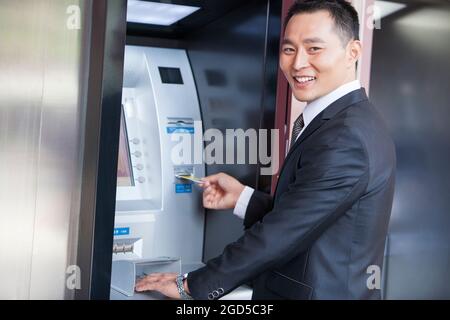 Homme d'affaires souriant utilisant un guichet automatique avec carte bancaire Banque D'Images