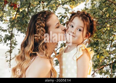 Maternité et maternité aimante. Belle jeune maman avec des cheveux tressés embrassant sa jolie petite fille douce dans la joue tout en passant du temps ensemble Banque D'Images