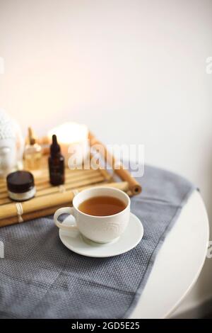 Table ronde dans le salon de spa avec une tasse de tisane à côté du plateau en bambou avec différentes huiles aromatiques et crèmes préparées après la procédure de traitement pour le rel Banque D'Images