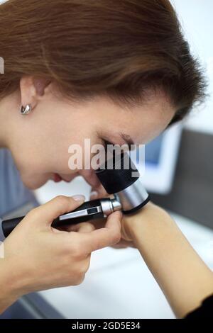 Photo en gros plan de la jeune femme brunette dermatologue examine le nevus ou les marques de naissance sur la main des patients avec le dermatoscope. Prévention du mélanome, de la mole con Banque D'Images