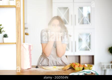 Jeune femme femme au foyer en tablier de la farine tout en faisant de la pâte et de la cuisine dans la cuisine légère à la maison, joueuse femme ayant le plaisir tout en faisant cuire la tarte pour f Banque D'Images