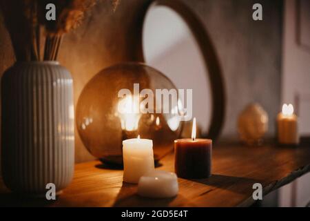 Miroir rond sur étagère en bois avec deux bougies allumées et petite tête de Bouddha en porcelaine réfléchie dans le coin de la surface en miroir sur le mur de béton Banque D'Images