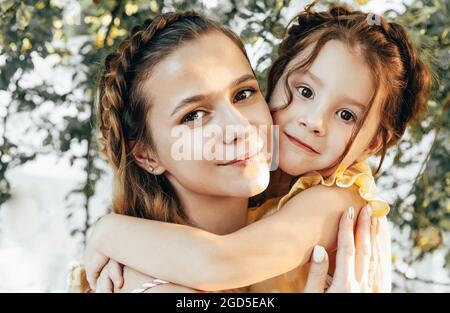 Maternité et maternité aimante. Belle jeune maman avec des cheveux tressés embrassant sa jolie petite fille douce tout en passant du temps ensemble à l'extérieur Banque D'Images