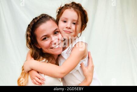 Maternité et maternité aimante. Belle jeune maman avec des cheveux tressés embrassant sa jolie petite fille douce tout en passant du temps ensemble à l'extérieur Banque D'Images