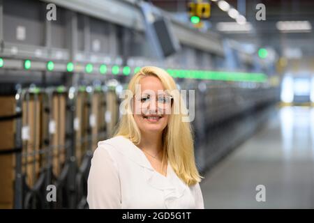 11 août 2021, Brandebourg, Stahnsdorf: Lara Küchenthal, responsable du centre de courrier et de colis de Deutsche Post, se trouve à côté du nouveau trieur multiformat. Depuis 25 ans, Deutsche Post utilise le centre pour livrer des lettres aux clients de la grande région de Potsdam et des quartiers sud-ouest de Berlin. En attendant, de moins en moins de lettres sont envoyées, mais d'autant plus de colis et de colis. Le système trie également ces colis de petit format avec une épaisseur maximale de dix centimètres et un poids de 2,000 grammes, qui peuvent ensuite être livrés dans le réseau de courrier par le transporteur de lettres. Photo: Soer Banque D'Images