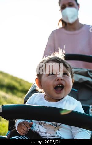 Petite fille en train de rire en profitant d'une promenade dans un parc assis dans la poussette moderne pendant l'épidémie de coronavirus - enfant doux en poussette montrant les premières dents dedans Banque D'Images