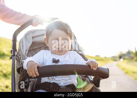 Joyeux rire petite fille en profitant d'une promenade dans la campagne assis dans la poussette moderne - enfant doux en buggy montrant les premières dents dans un grand rire - Tra Banque D'Images