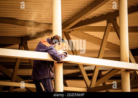 Un soudeur dans un masque de soudage, un uniforme de construction et des gants de protection prépare une machine à souder en métal sur la construction de rue. Vue arrière, perso non reconnaissable Banque D'Images