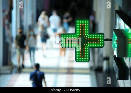 La croix verte de la pharmacie et le symbole de la médecine un navire avec un serpent mis au-dessus de l'entrée de la pharmacie, les gens flous marchant sur un fond. Banque D'Images