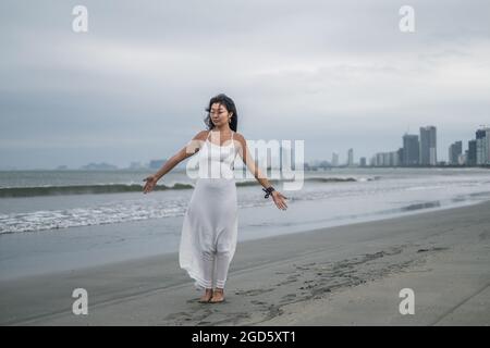 Charmante jeune femme asiatique en robe blanche se tient avec les mains sur le côté de la plage. Photo romantique et paisible. Photo de haute qualité Banque D'Images