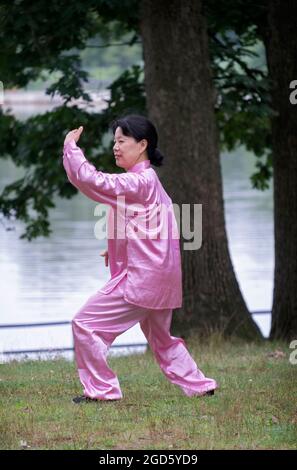 Une femme attirante dans un costume de Tai Chi rose brillant passe par des mouvements gracieux dans un parc à Queens, New York City Banque D'Images