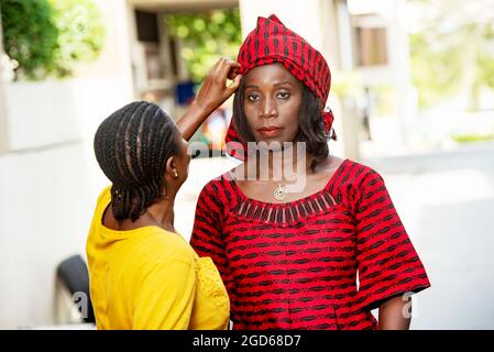 femme africaine mûre debout à l'extérieur regardant la caméra tandis que sa sœur ajuste son foulard. Banque D'Images