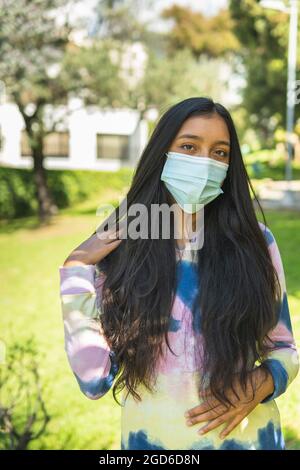 Latin teen fille avec long droit cheveux noirs port masque regardant l'appareil photo Banque D'Images