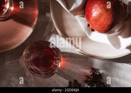 Tisane aux fruits chauds dans un verre sur une assiette de table grise, grenade mûre, vapeur qui s'élève du verre, lumière dure avec des ombres dures, vue du dessus Banque D'Images