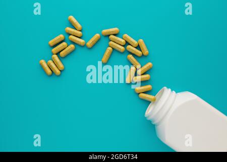 capsules de compléments alimentaires jaunes déversées hors du pot blanc sans marque sur fond turquoise. maquette de bouteille médicale. modèle médical pour la marque Banque D'Images