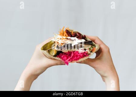 Gros plan des mains tenant le shawarma végétarien avec des haricots rouges et des cornichons enveloppés de pain pita Banque D'Images