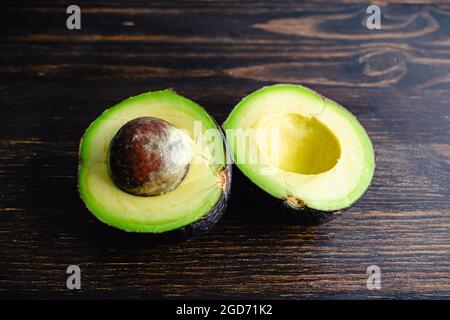 Moitié Haas Avocado sur un bois sombre fond: Haas Avocado coupé en moitié avec la fosse encore en une seule pièce Banque D'Images