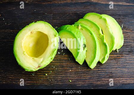 Haas Avocado pelé et tranché sur un bois foncé fond: Tranches de Haas Avocado sur une planche à découper en bois Banque D'Images