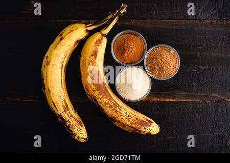 Bananes poêlées à la cannelle Ingrédients sur une table en bois : bananes surmûres, cannelle, sucre et muscade sur fond de bois sombre Banque D'Images
