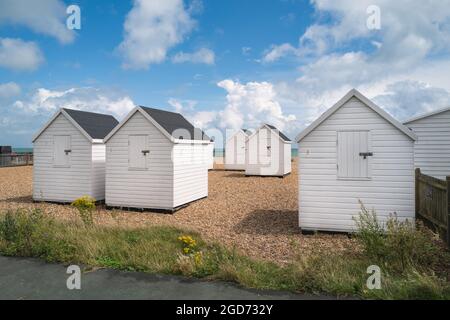 Cabanes de plage blanches sur une plage de galets avec un ciel bleu et des nuages blancs. Banque D'Images