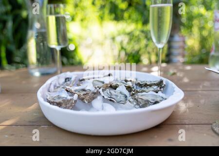 Un gros plan d'huîtres fraîches ouvertes et de coquillages avec des quartiers de citron, deux verres de vin blanc ou de champagne sur une table extérieure Banque D'Images
